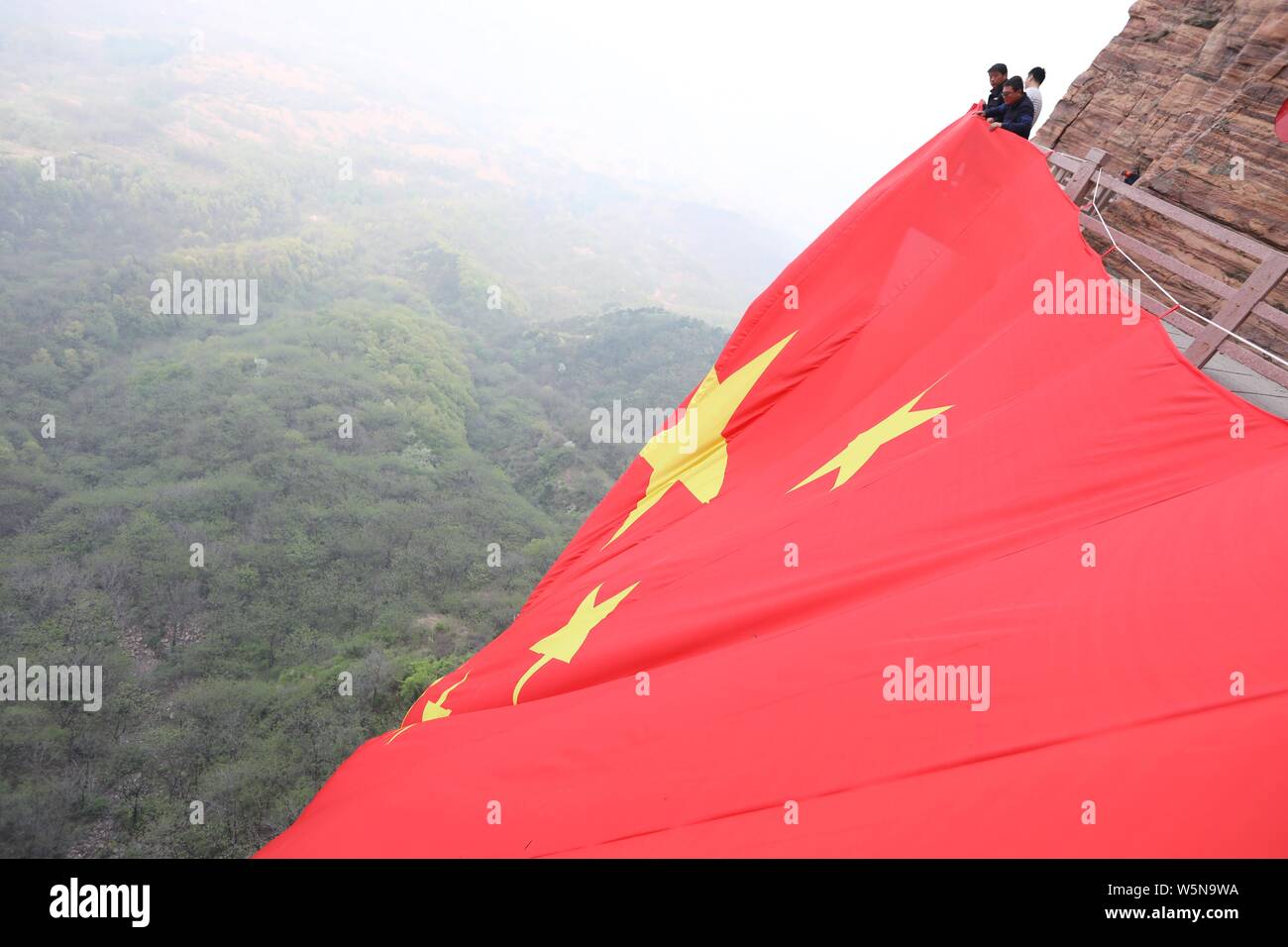 Los trabajadores chinos colgar una enorme bandera nacional para conmemorar el 70º aniversario de la fundación de la República Popular de China a lo largo de un acantilado en el Taihang Foto de stock