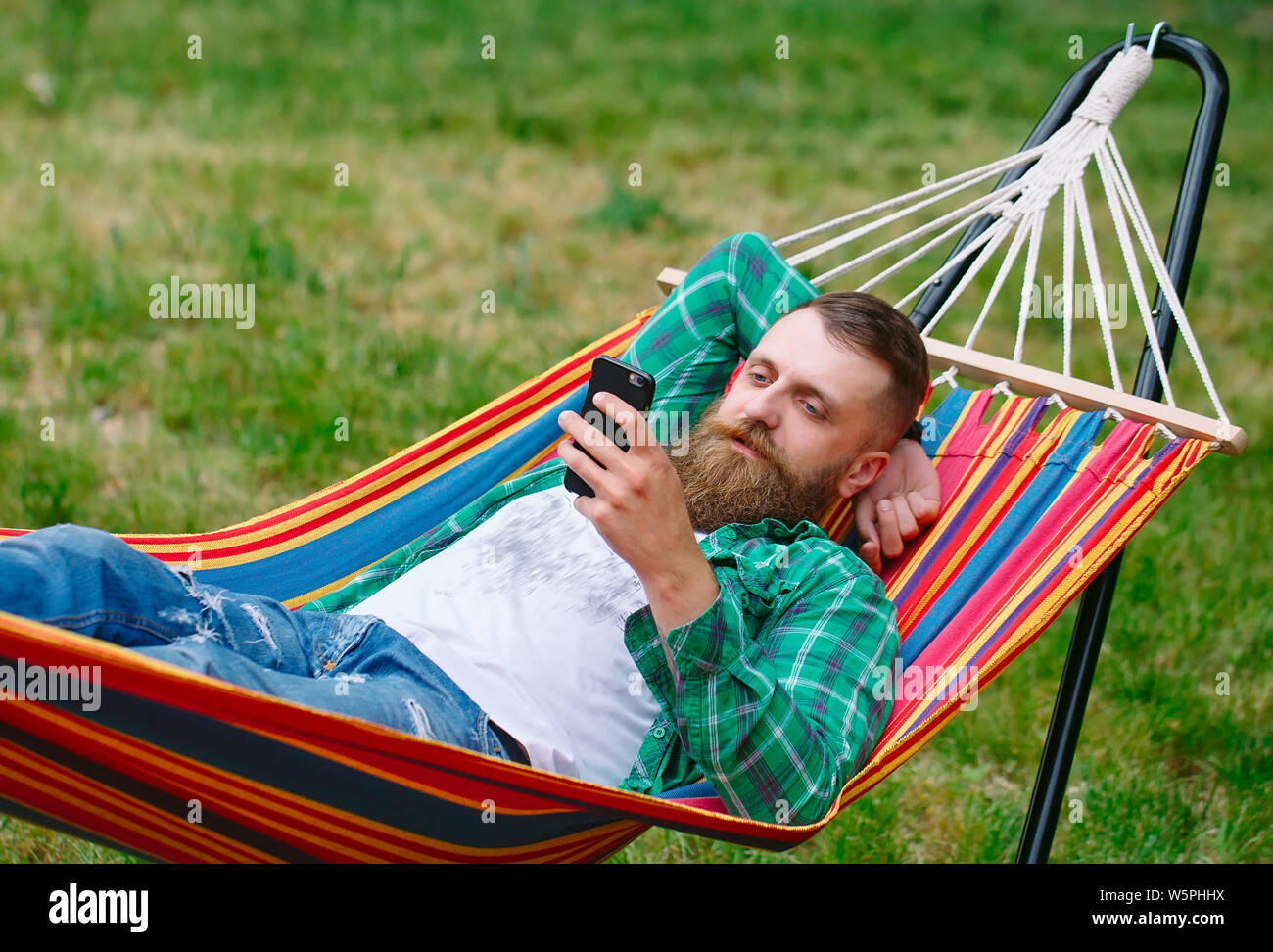 Hombre utilizando una aplicación en su teléfono móvil blanco balanceándose  en una hamaca Fotografía de stock - Alamy