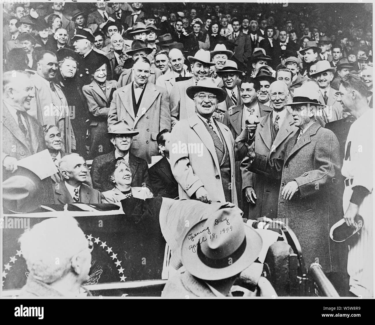 Fotografía del presidente Truman y sonriente sosteniendo la pelota de béisbol que él está a punto de tirar para abrir la temporada de beisbol en Griffith Stadium en Washington, como la Sra. Truman y otros dignatarios. Foto de stock