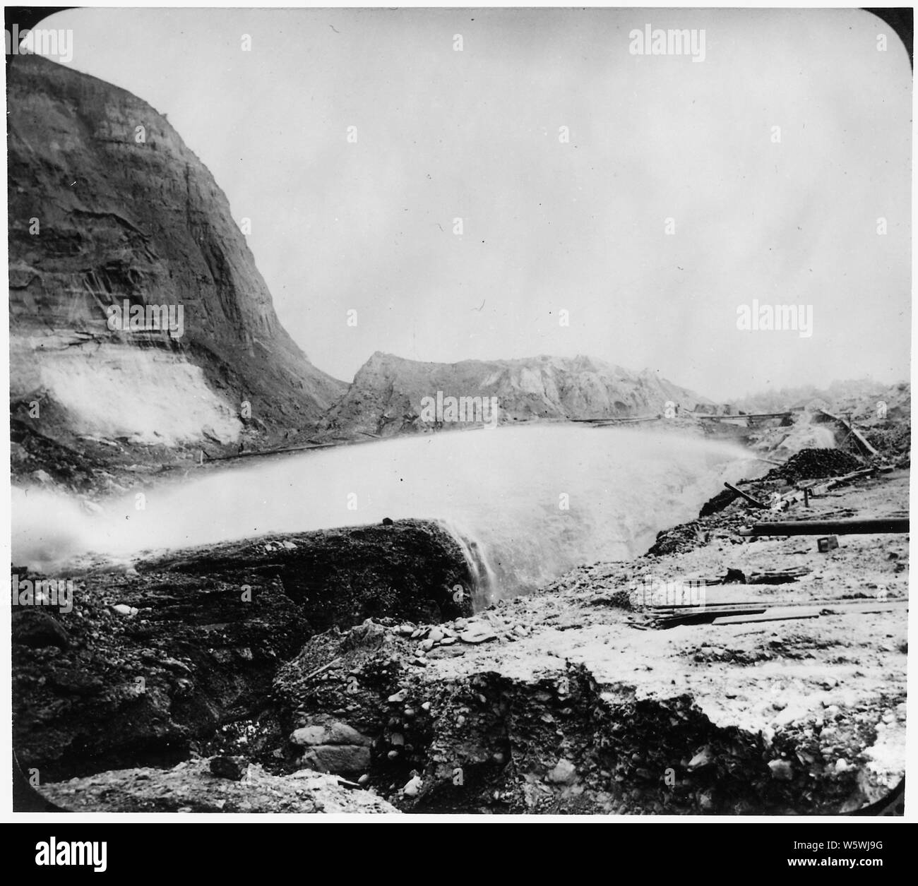 Fotografía de una operación minera hidráulica mediante el cual el agua se atacó contra la ladera para separar estructuras de rocas sueltas y usurpan los depósitos de oro. Cañón de agua puede verse a la derecha disparar a través de un abismo a un terraplén a la izquierda; el alcance y contenido: No hay ninguna ubicación dada para este photgraph, pero se supone que la mina se encuentra en California ambientalmente devastada Sierra Nevada. Foto de stock