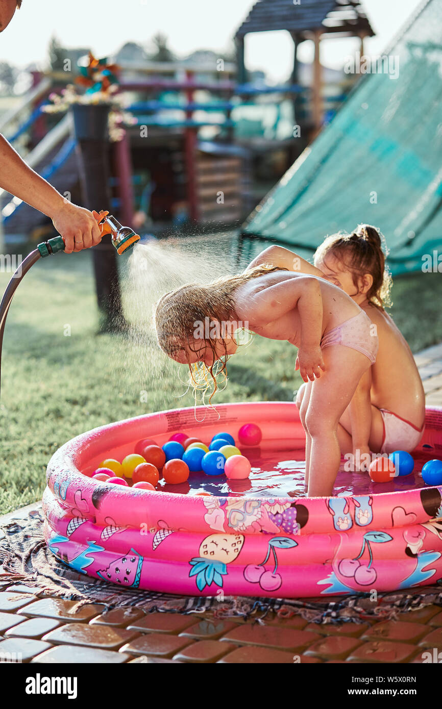 Poco cute adorables chicas disfrutar de una fresca agua salpicada por su  padre durante los calurosos días de verano en el jardín. Personas sinceras,  momentos reales, auténticos sit Fotografía de stock -