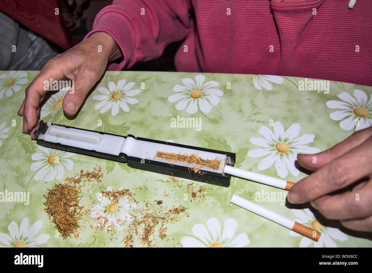 Hacer los cigarrillos y tabaco mediante rodillos hechos a mano sobre una mesa en casa. Foto de stock