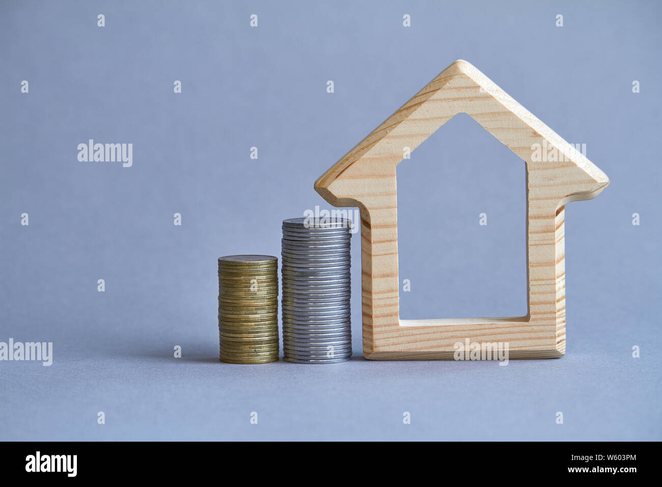 Figurilla de madera casa con dos columnas de monedas cerca sobre fondo gris, el concepto de la compra o el alquiler de un edificio, el enfoque selectivo Foto de stock