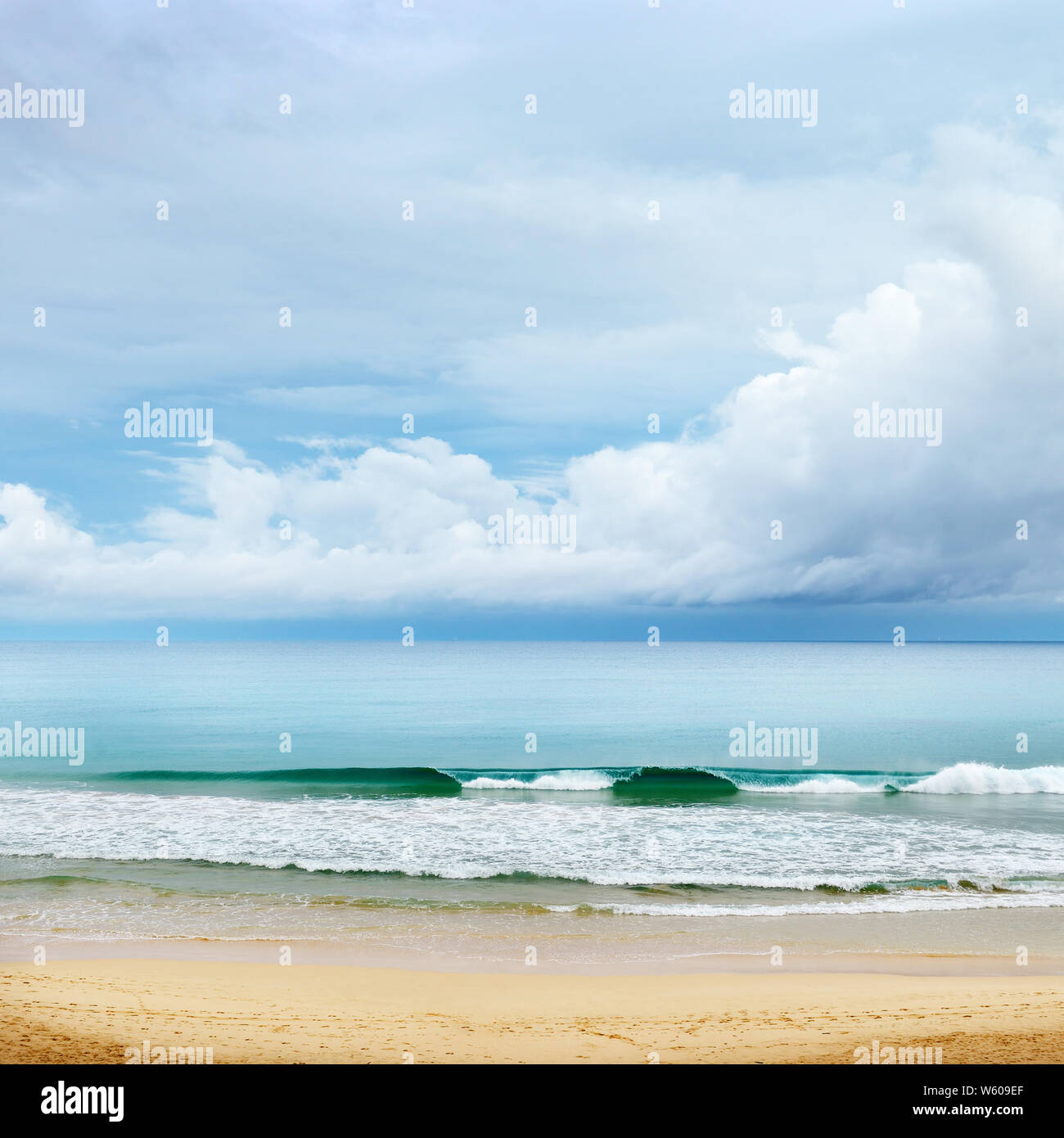 La costa de la playa de arena, olas altas y las nubes blancas en el cielo azul Foto de stock