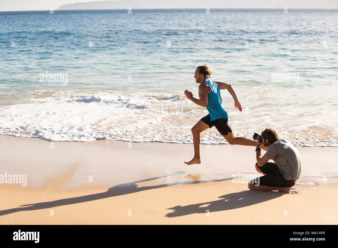 Detrás de las escenas de la sesión de fotos de deportes masculinos modelo atleta corriendo de fotógrafo tomando fotos para el deporte photoshoot. El BTS en la playa. Foto de stock