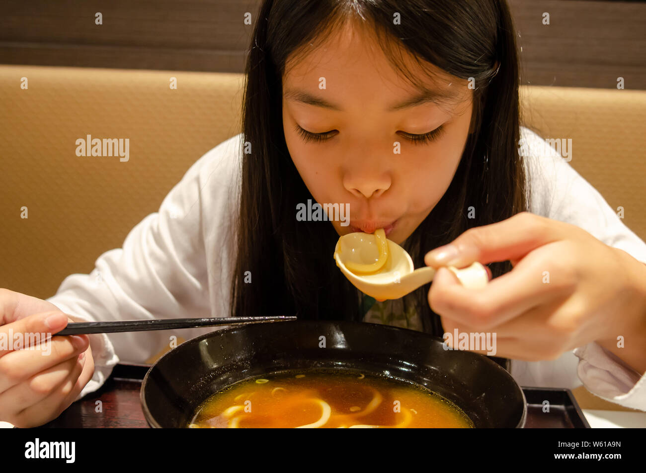 Mujer joven usando palillos y cuchara para comer ramen sabroso Mientras  estaba sentado en una mesa en un restaurante japonés Fotografía de stock -  Alamy
