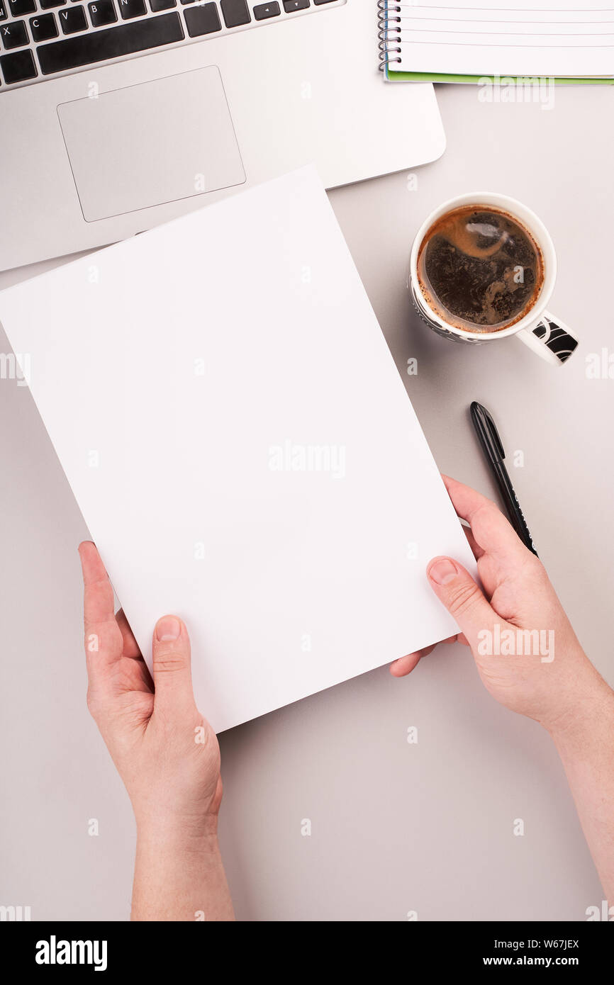 Las manos del hombre la celebración de papel en blanco sobre la mesa de trabajo con ordenador y café Foto de stock