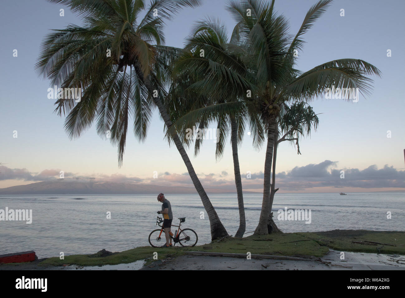 Temprano por la mañana con una persona irreconocible en una bicicleta en la isla tropical de Maui. Foto de stock