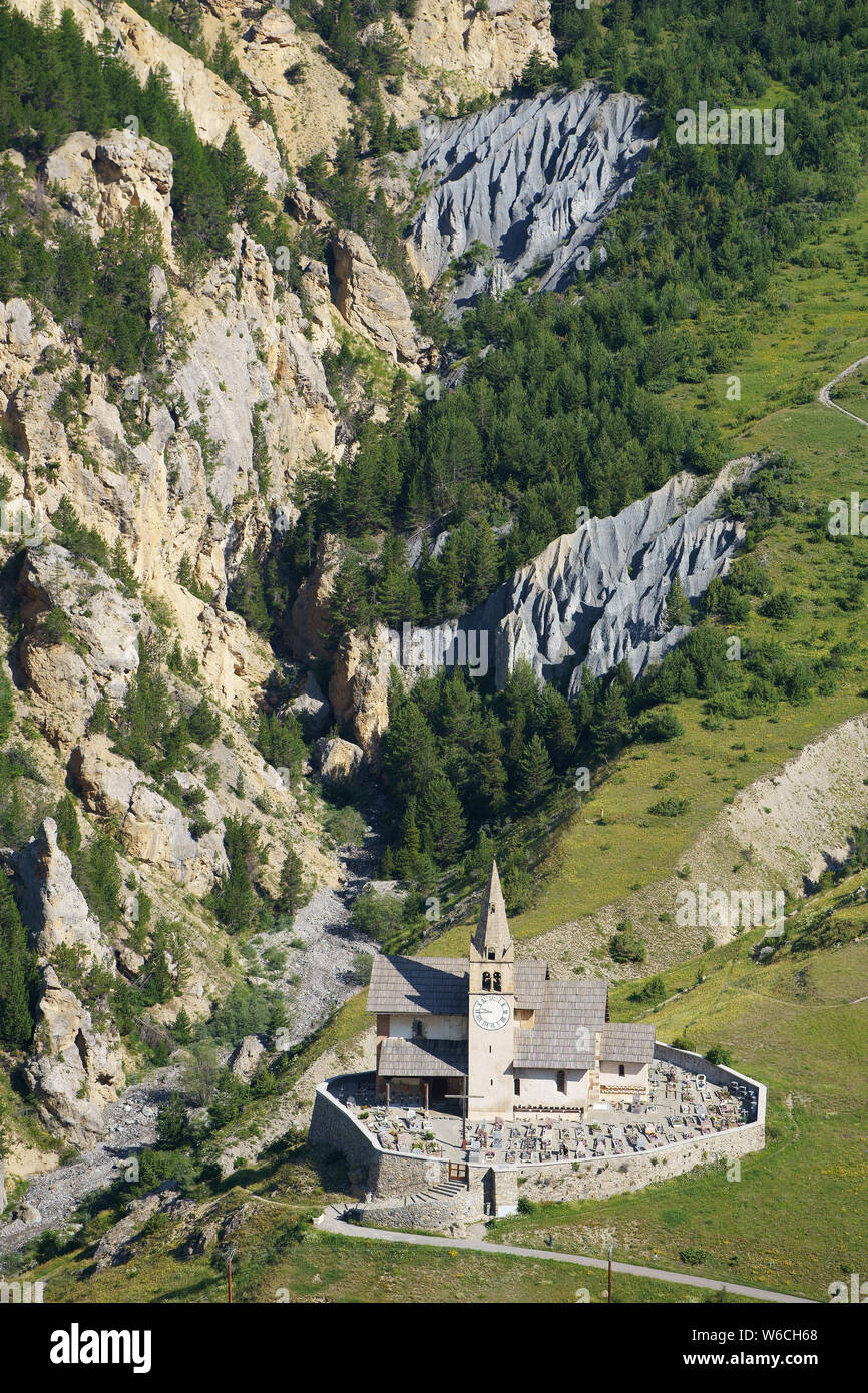 VISTA AÉREA. Remota Iglesia de Saint-Michel y cementerio con un pintoresco cañón de fondo. Cervières, Altos Alpes, Francia. Foto de stock