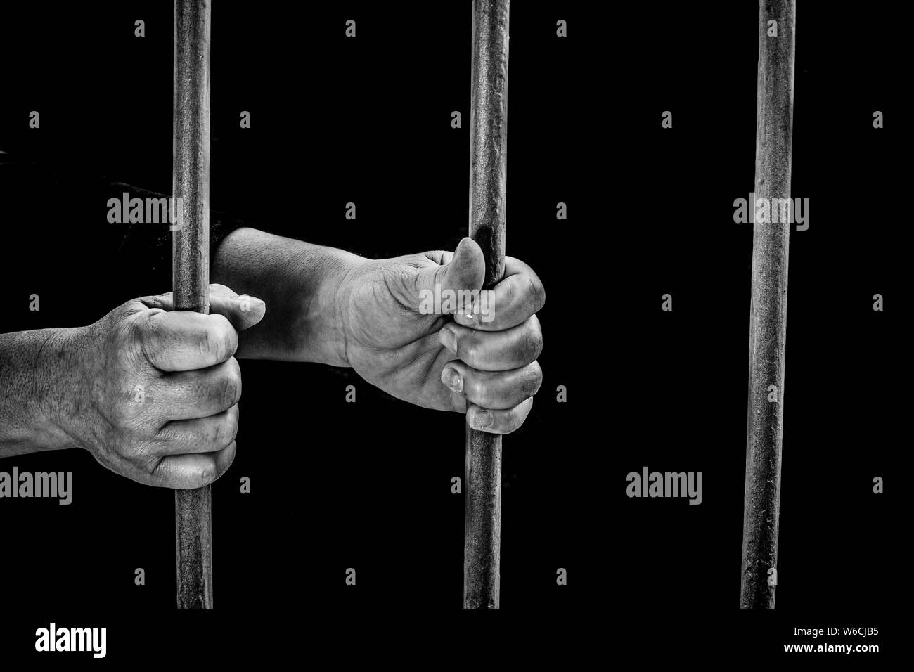 Encarcelado en una prisión oscura sujetando los barrotes de la celda de una prisión en espera de la justicia Foto de stock
