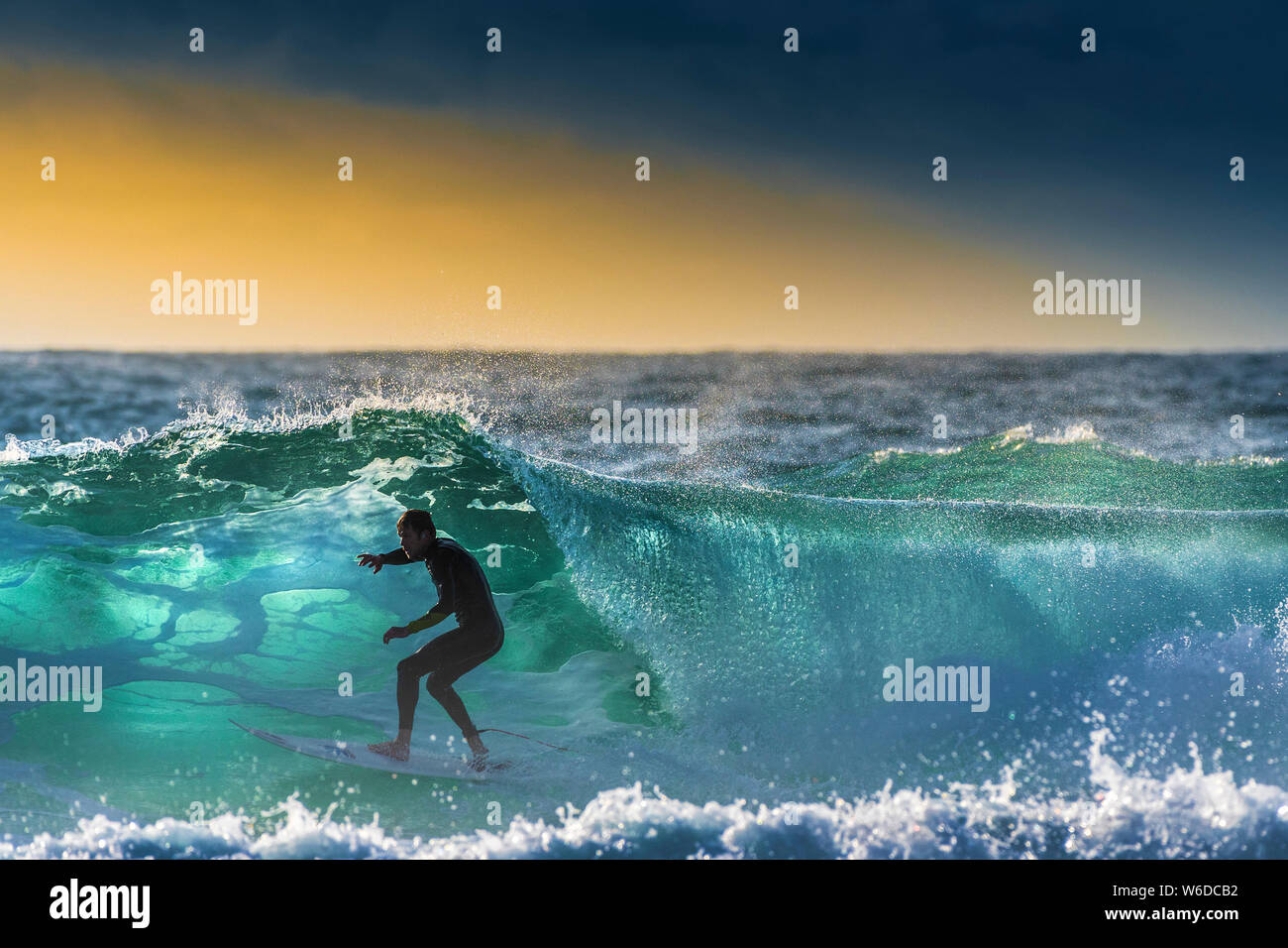 Un surfista cabalgando una ola retroiluminada por la puesta de sol en Fistral en Newquay en Cornualles. Foto de stock