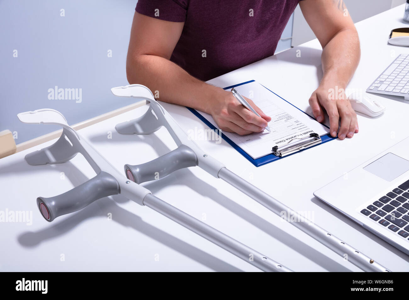 Paciente masculino de discapacitados rellenando el formulario de reclamación de seguros sobre la mesa con muletas Foto de stock