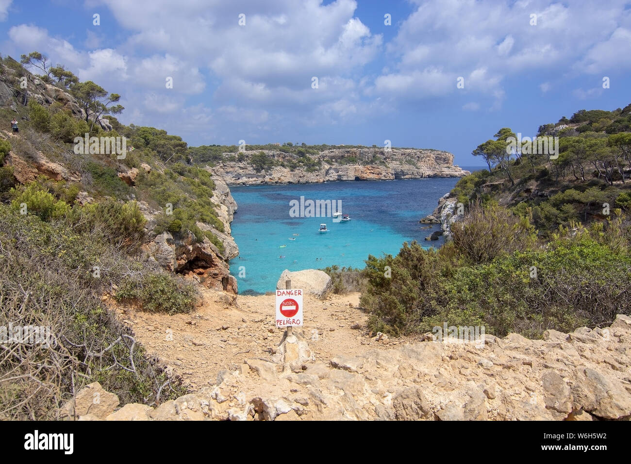 CALO DES MORO, Mallorca, España - Julio 27, 2019: señal de peligro por extremadamente pequeña bahía de aguas turquesas y acantilados escarpados en un día soleado en Julio 27, 2019 En Calo Foto de stock