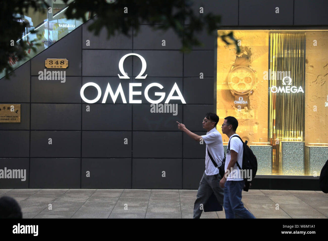 --FILE--peatones caminar pasado un anuncio de relojes Omega en Shanghai, China, 30 de agosto de 2017. Los relojeros en la feria más importante del sector en el gen Foto de stock
