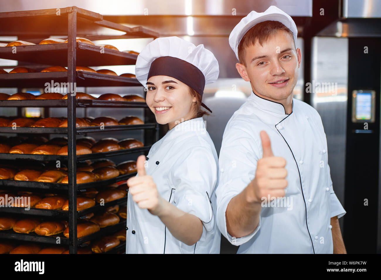 Chico y chica panaderos en el fondo de un horno industrial en una panadería  mostrar pulgar arriba Fotografía de stock - Alamy