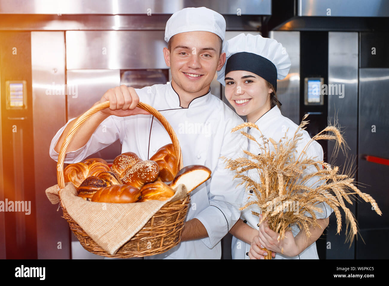 Panaderos chico y chica con una cesta de cocción y spikelets de trigo  contra el telón de fondo de un horno industrial en una panadería Fotografía  de stock - Alamy