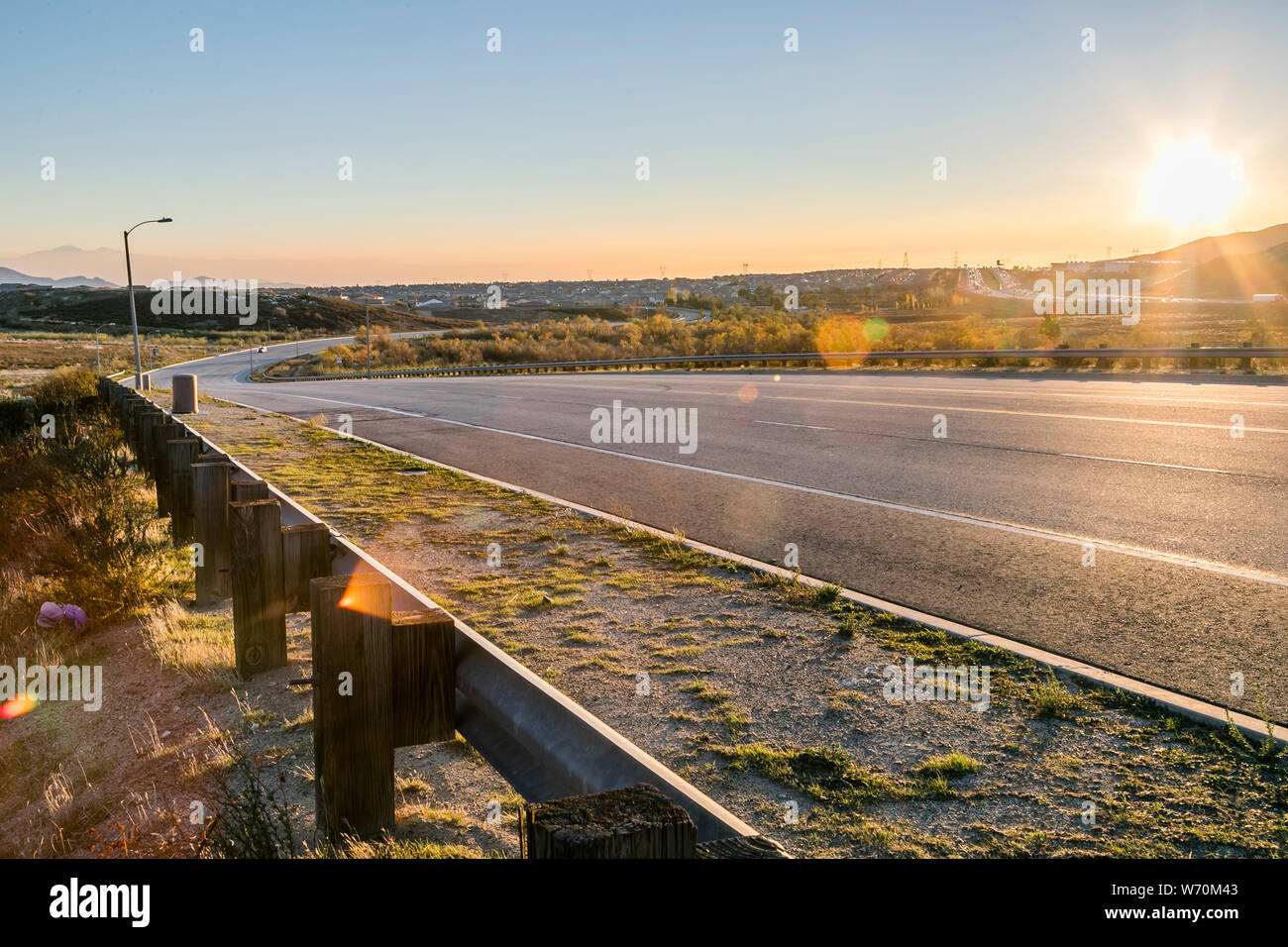 Calle rural asfaltada y calzada con curva y barandilla en luz dorada Foto de stock