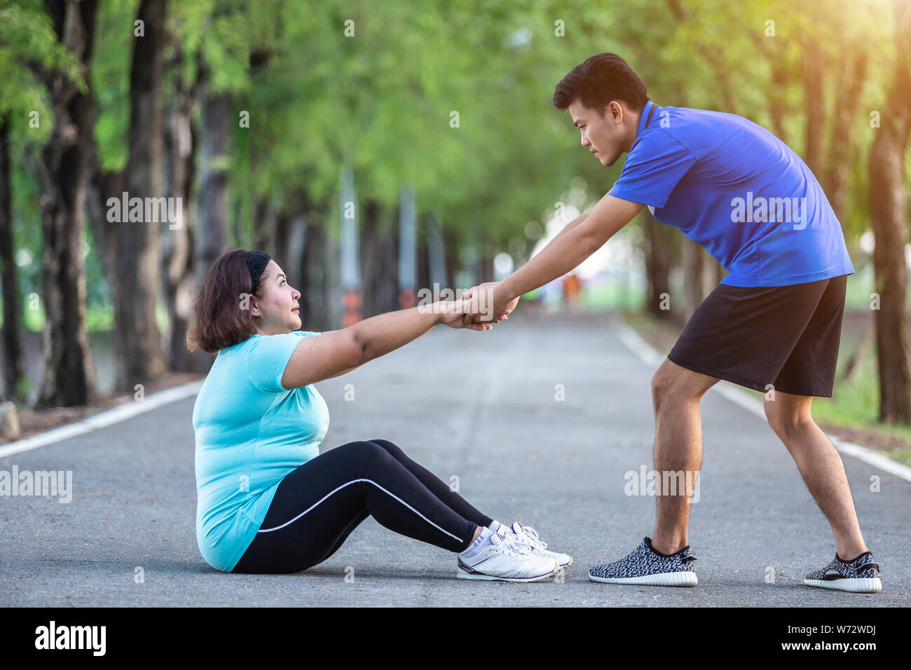 Hombre asiático tirando mano y dar aliento a fat mujer que cansados y sentados en el suelo Foto de stock