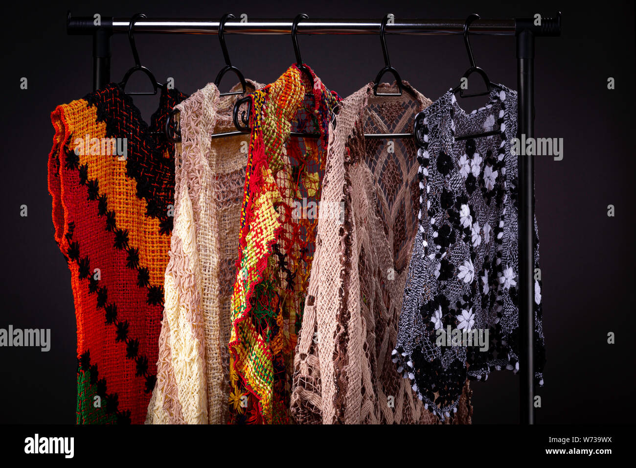 Cerca de coloridos bordados armario con un arco iris vestidos y chalecos sobre un estante percha contra un fondo gris limpio Fotografía de stock - Alamy