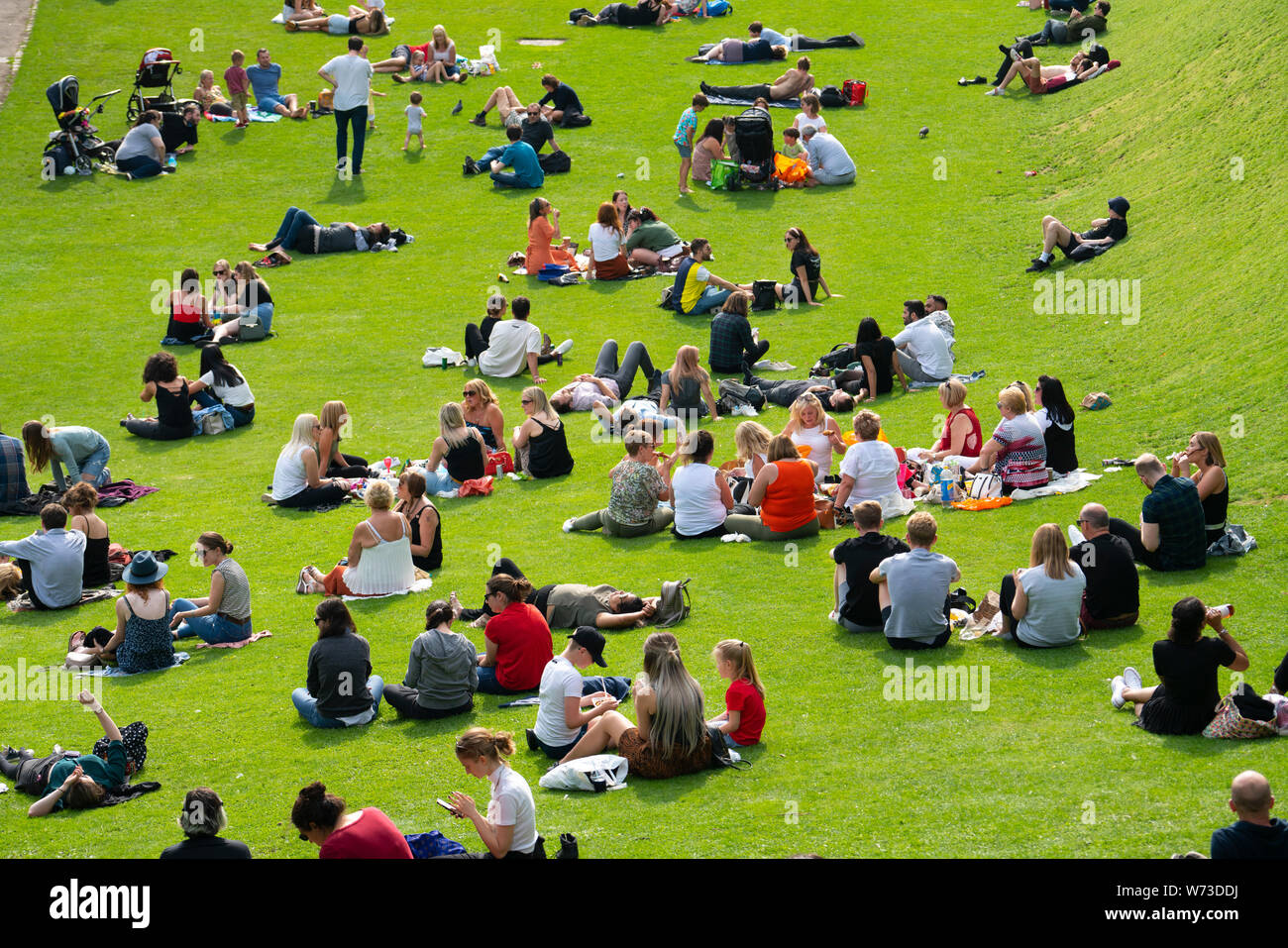 Personas sentadas en el césped en los jardines de Princes Street en verano caluroso en Edimburgo, Escocia, Reino Unido Foto de stock