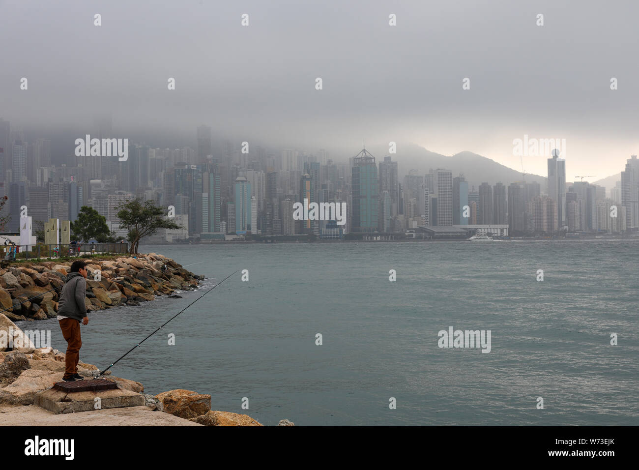 Hombre con una caña de pescar en Yau Ma Tei, rascacielos de la isla de Hong Kong en el backgroung, en un día de niebla Foto de stock