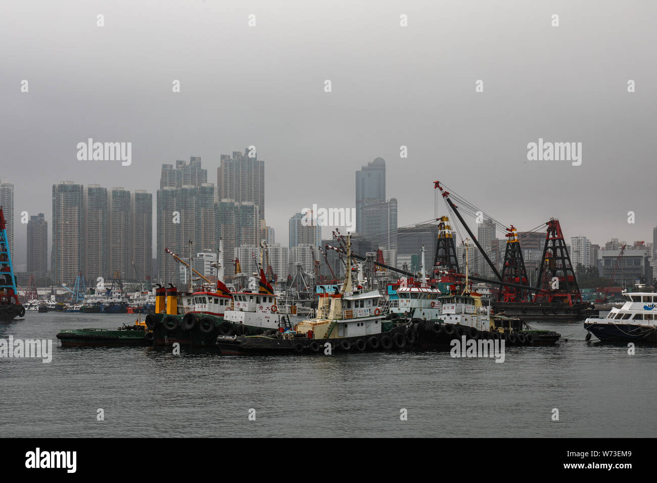 Contenedor de remolcadores y barcazas con grúas derrick en un día brumoso en Yau Ma Tei, Hong Kong Foto de stock