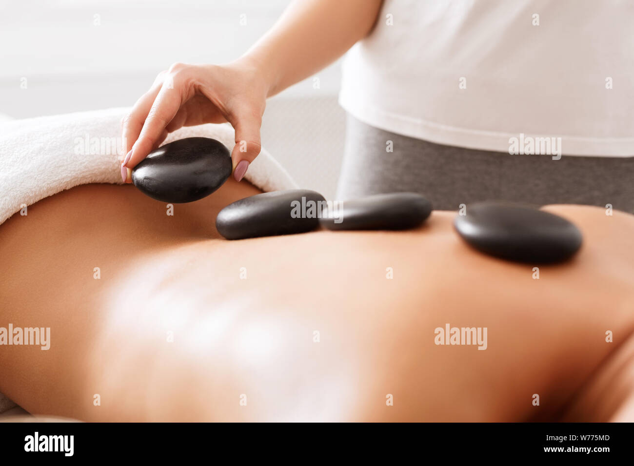 Masajista haciendo masaje de piedras calientes a la clienta Foto de stock