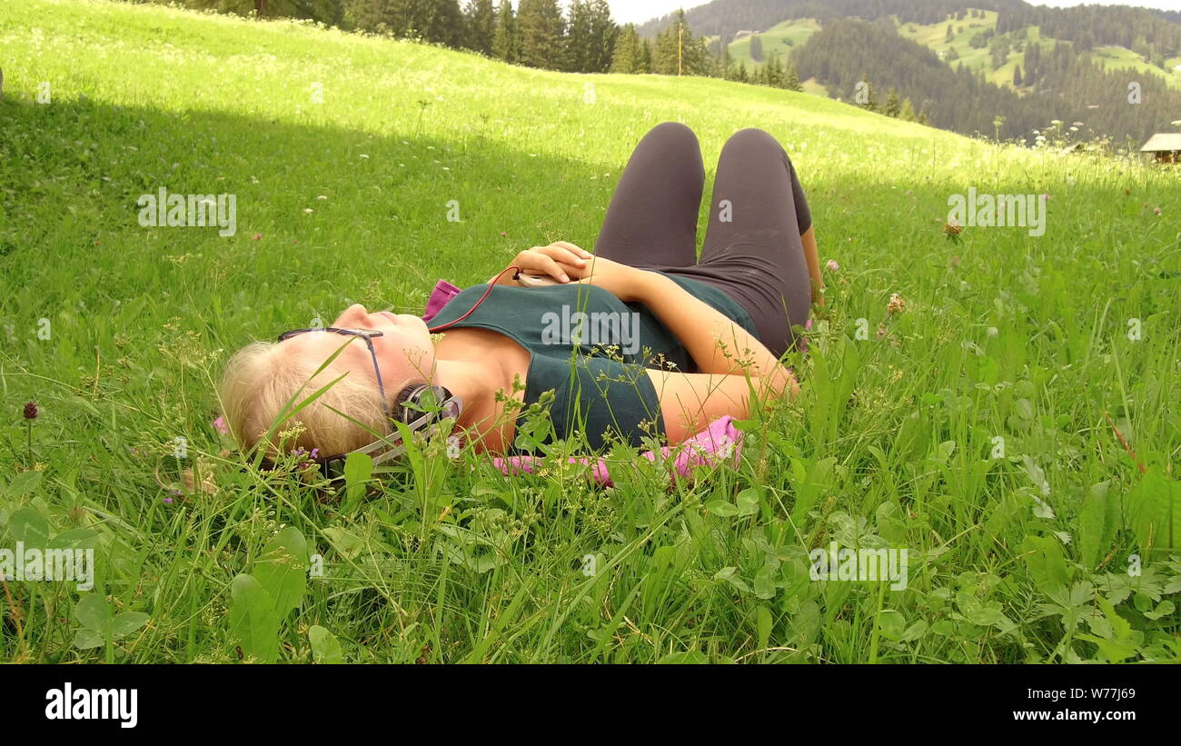 Chica rubia escucha música con auriculares en un césped verde Foto de stock