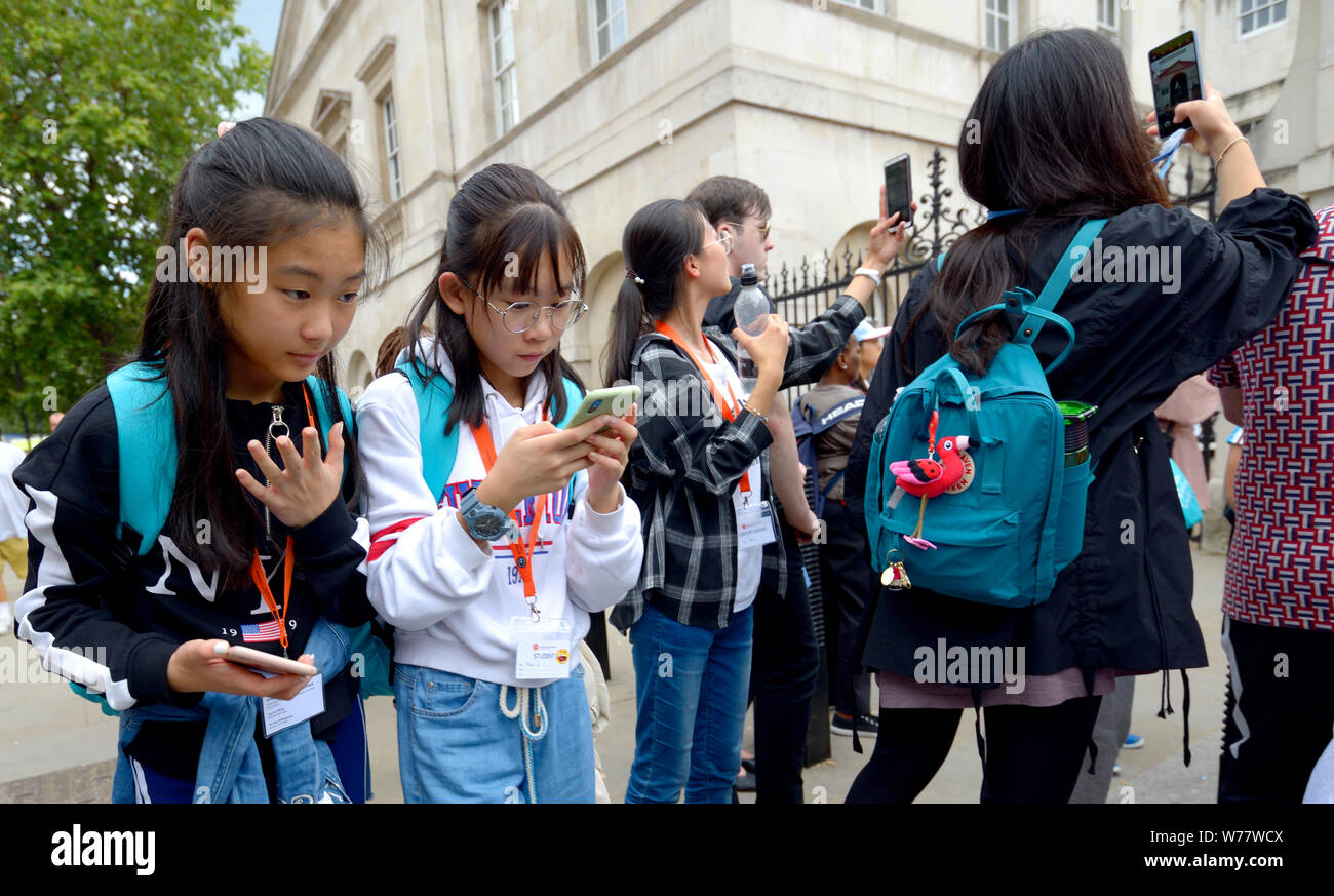Londres, Inglaterra, Reino Unido. Los jóvenes turistas japoneses en Whitehall mirando sus teléfonos móviles Foto de stock