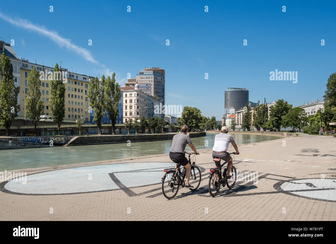 Dos personas de mediana edad en bicicletas, ciclismo junto al canal del Danubio (Donaukanal) en el centro de Viena, Austria. Foto de stock