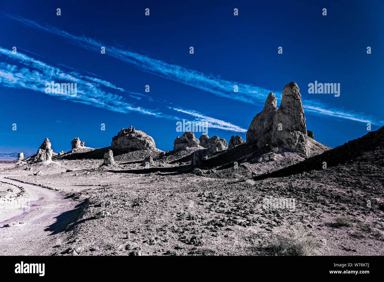Camino de tierra que conduce a través de yermo desolado paisaje desértico con pináculos y formaciones rocosas en blanco y negro bajo el cielo azul con nubes blancas. Foto de stock