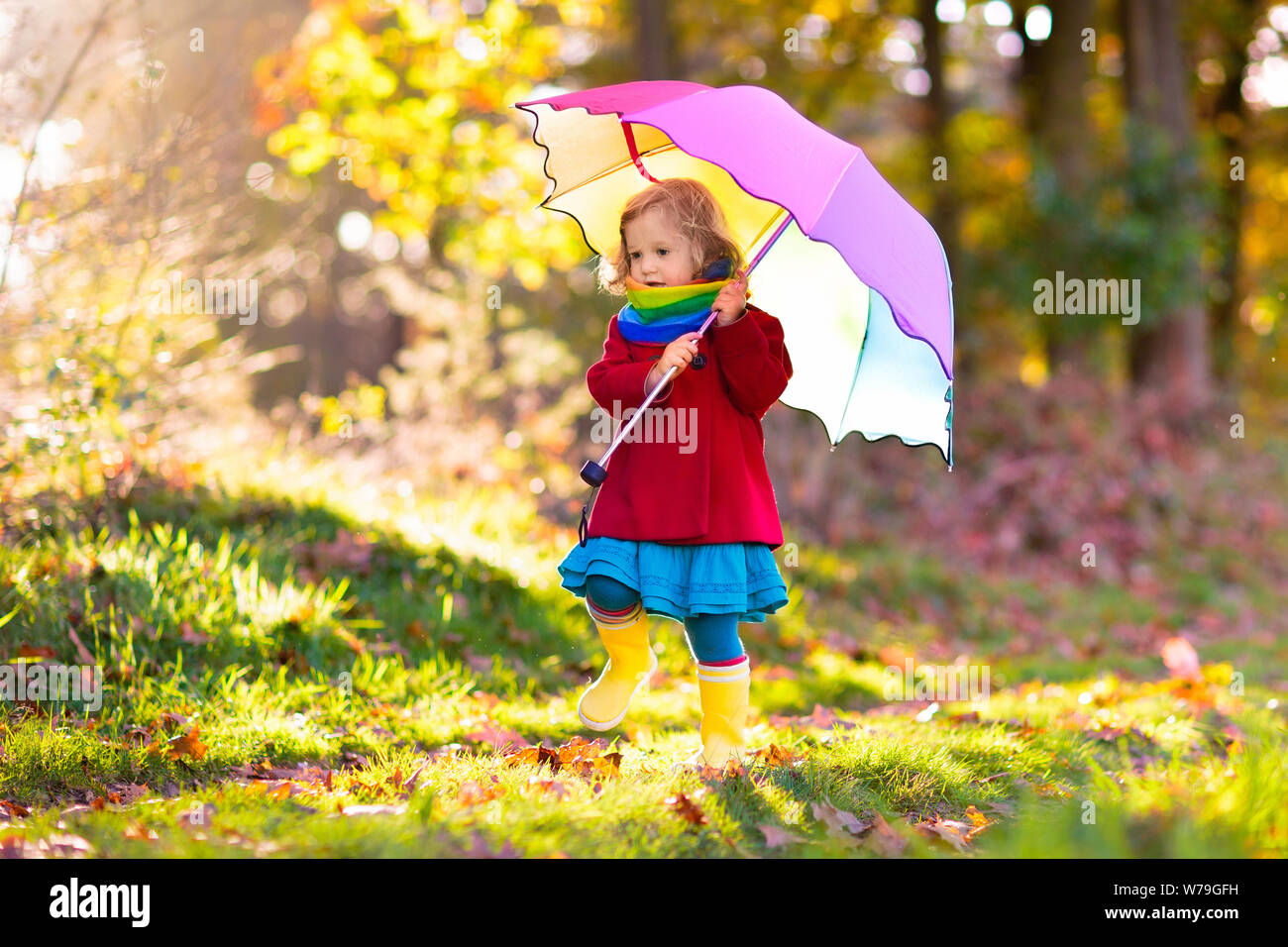 Kid jugar afuera en la lluvia. Los niños con paraguas y botas de lluvia  juegan al aire libre en otoño pesada lluvia. Niña saltando en charcos de  barro. Los niños divertida b