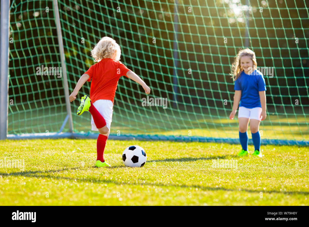 Los niños juegan al fútbol en el campo al aire libre. Los niños un gol en el partido fútbol. Niños y niñas patear la pelota. Niño corriendo en el equipo de