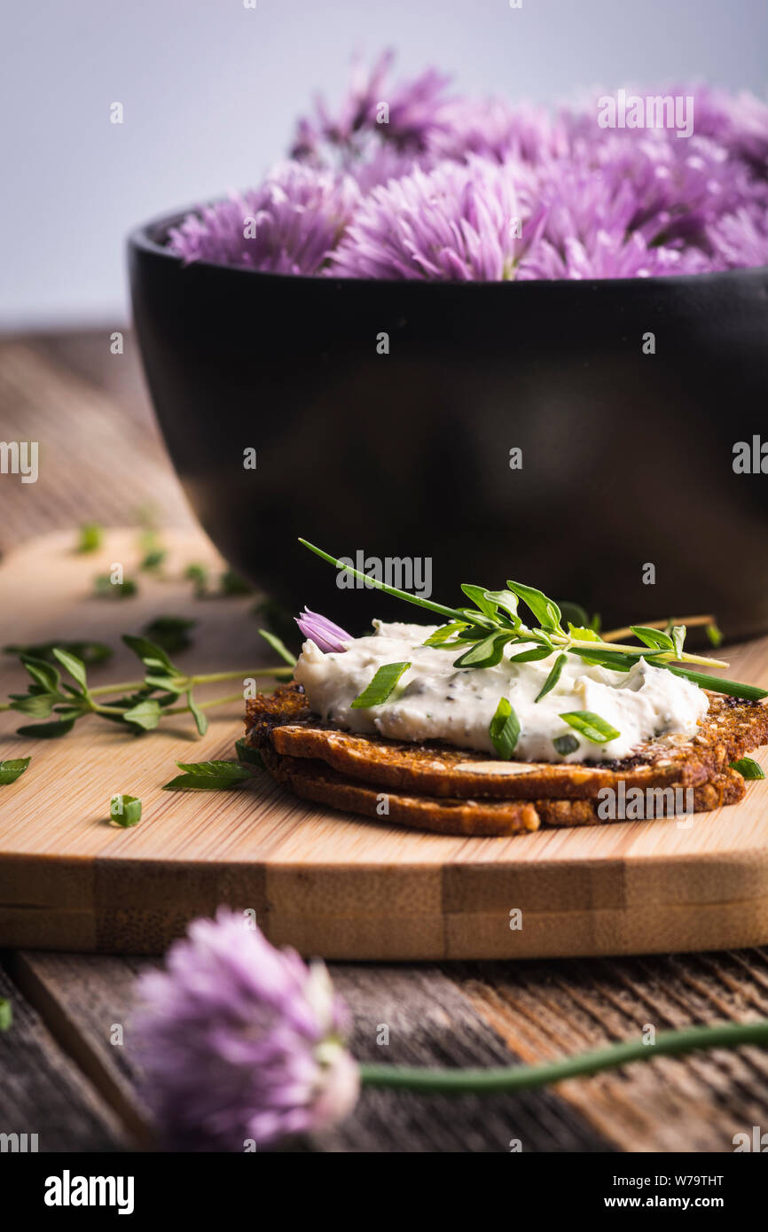 Una deliciosa crema de cebollino de ajo y queso para untar sobre galletas herbed junto a un tazón de flores púrpura de cebolleta. Foto de stock