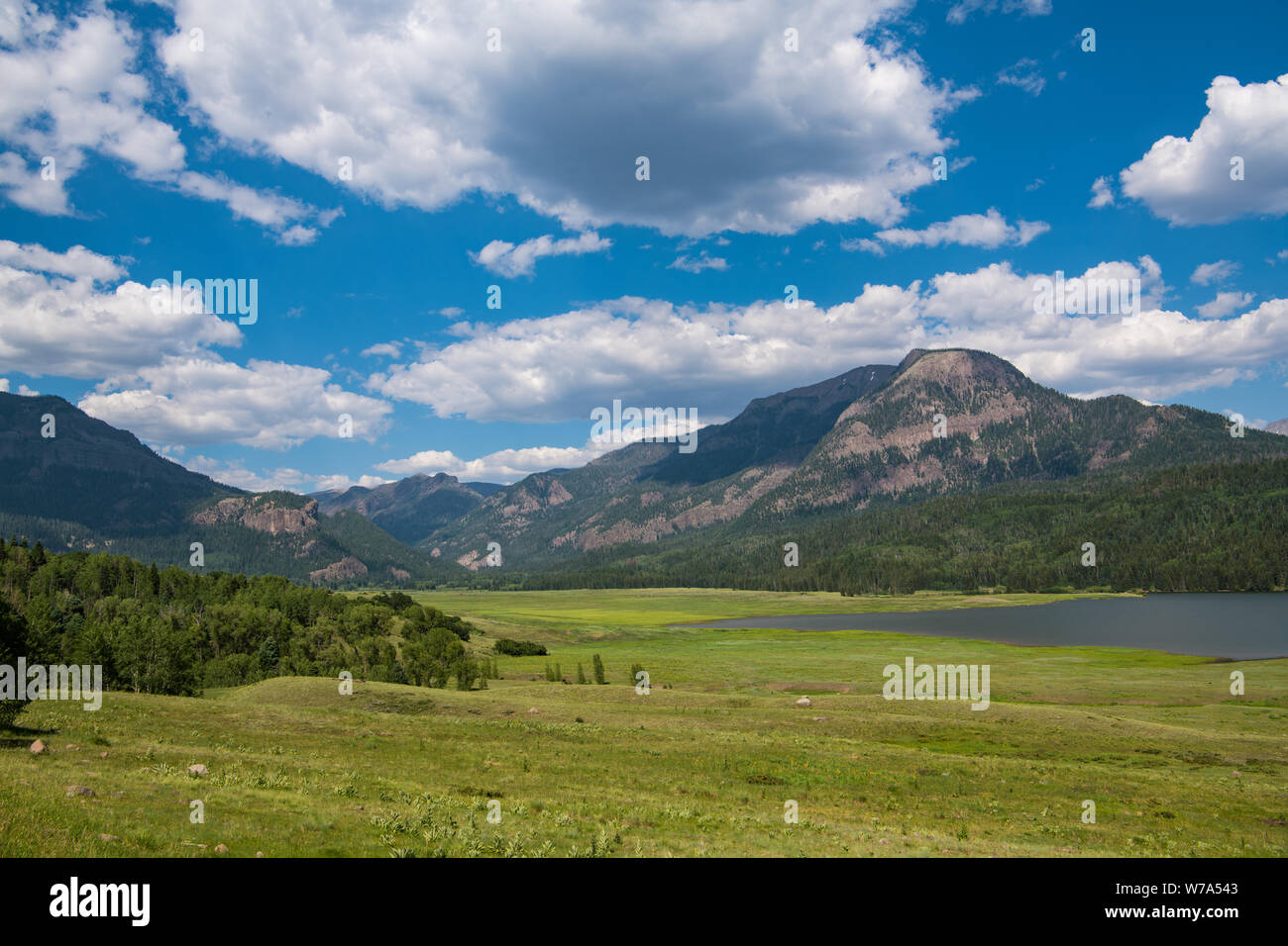 Exuberantes y verdes praderas y lago debajo de las Montañas Rocosas y un cielo azul con nubes blancas cerca de Pagosa Springs, Colorado Foto de stock