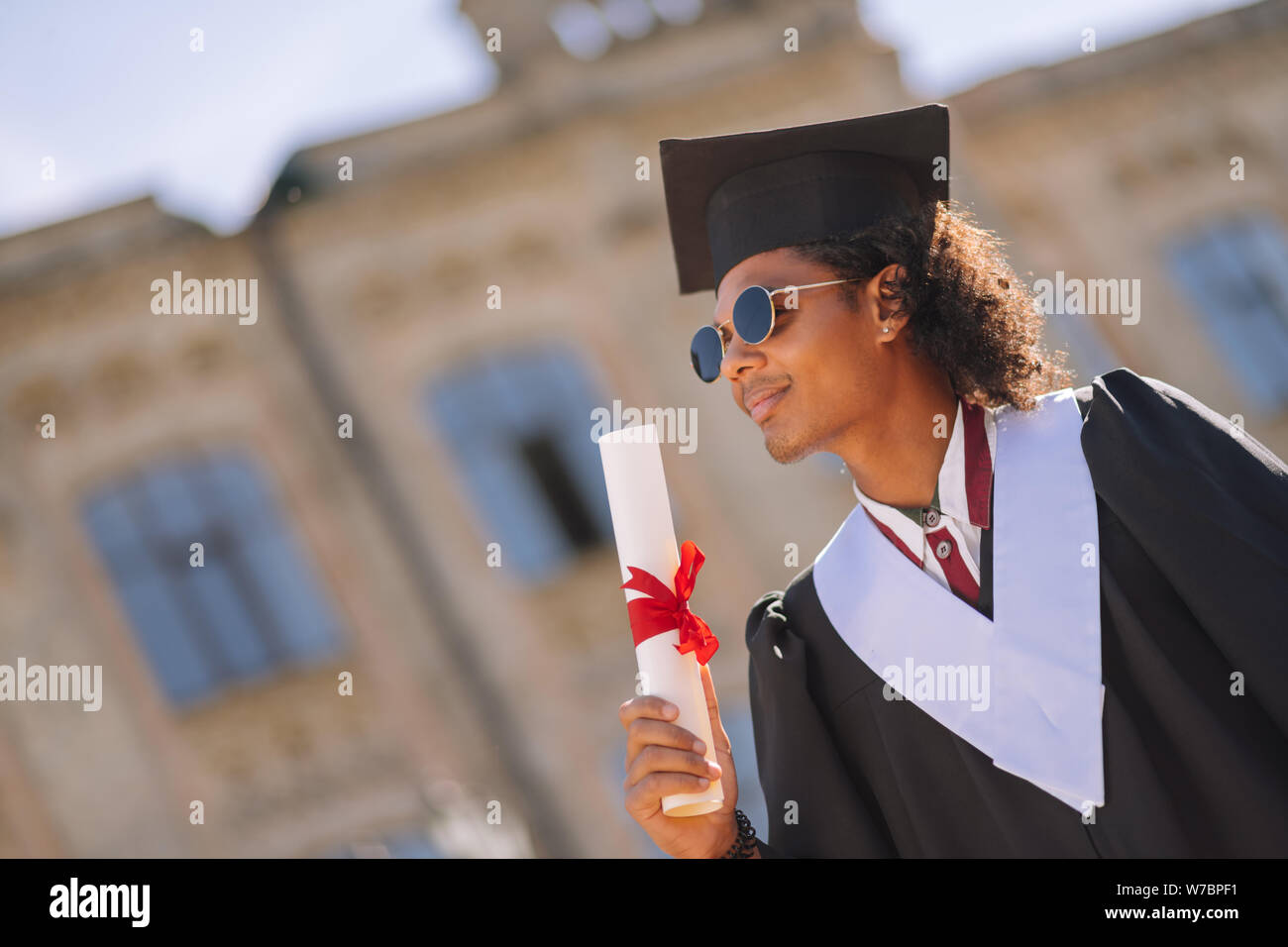 Perpleja graduand de pie delante de su universidad. Foto de stock