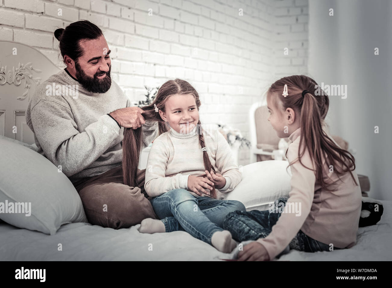 Padre haciendo sus hijos trenzas sentada en la cama Foto de stock