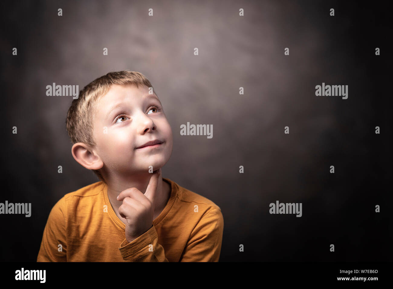 Retrato de estudio de un niño de 6 años mirando hacia arriba con una expresión pensativa. Foto de stock