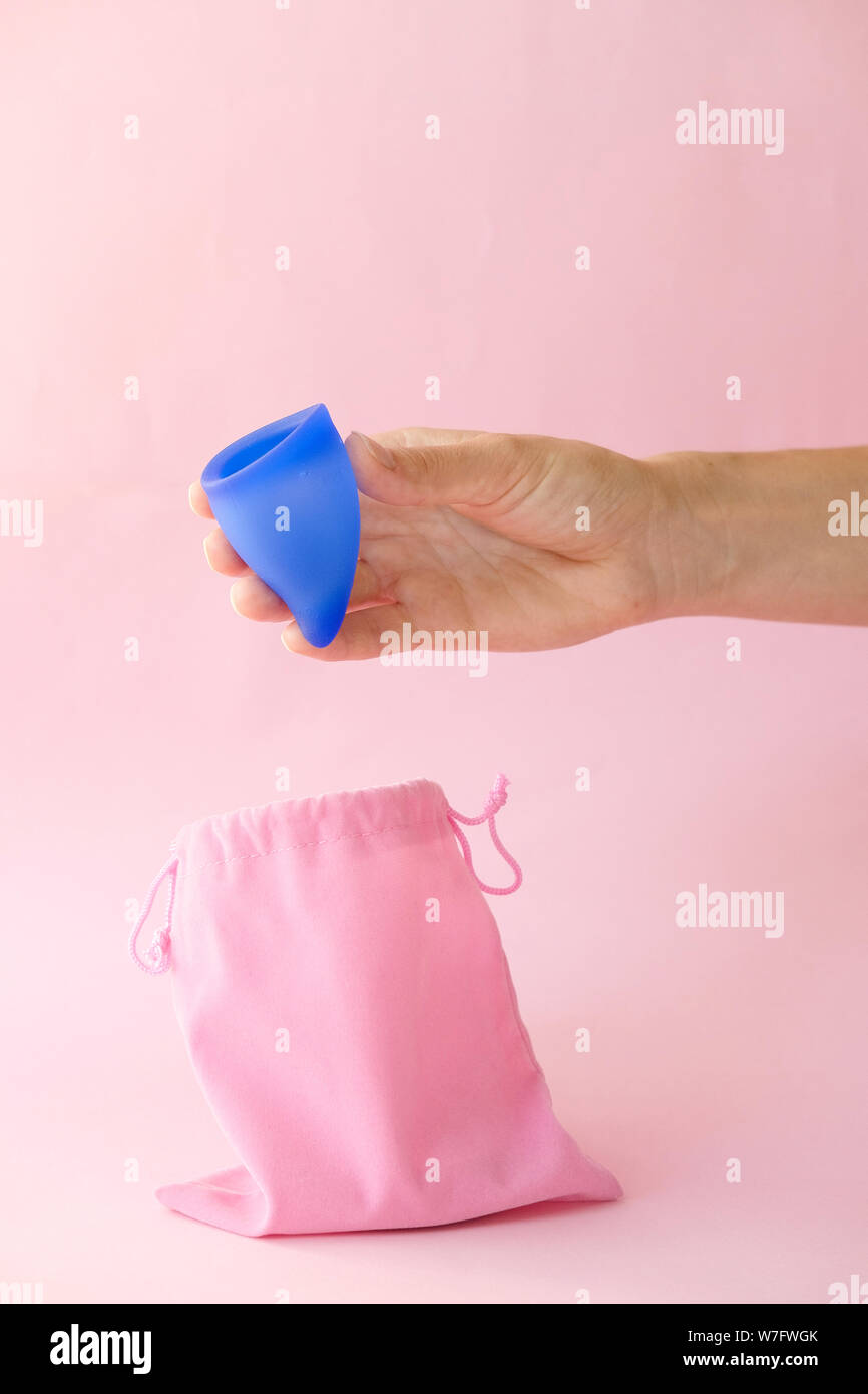 Lado femenino con taza menstrual y bolsa azul sobre fondo de color rosa. Producto alternativo para la higiene femenina, en lugar de tampones durante el período. La menstruación, cr Foto de stock