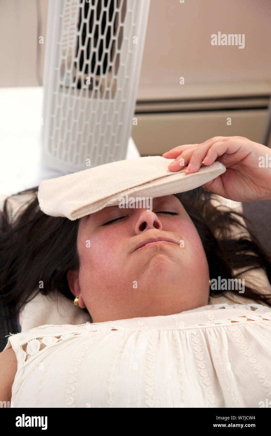 Mujer fija en la parte frontal del ventilador con una bolsa de hielo sobre  su frente en un día swealtering Fotografía de stock - Alamy