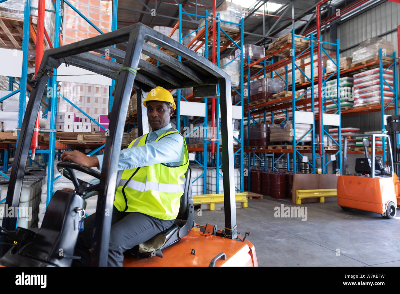 Trabajador masculino mirando a la cámara mientras conduce la carretilla en el almacén Foto de stock
