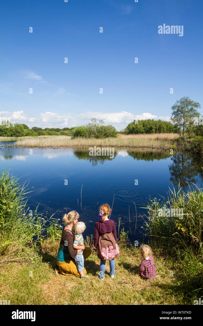 Familia disfrutando de una excursión a la Reserva Natural Shapwick Heath, mirando por encima del agua. Parte de las marismas de Avalon complejo que se ha creado a partir de la extracción de turba obras abandonadas. Los niveles de Somerset, cerca de Glastonbury, Reino Unido, junio de 2014. Modelo liberado. Foto de stock