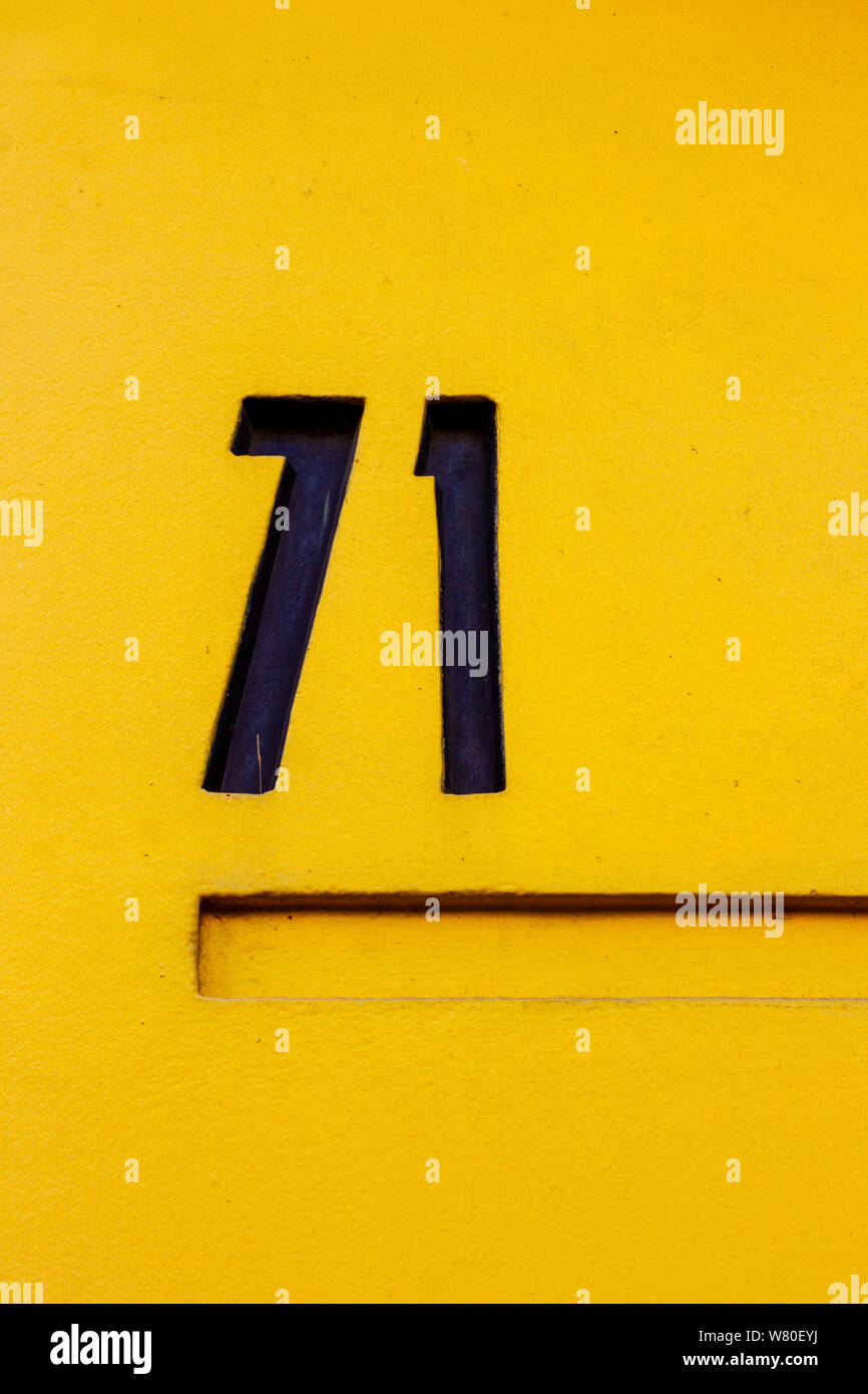 Bold casa número 71 en negro en un brillante amarillo canario con subrayado de la puerta Foto de stock