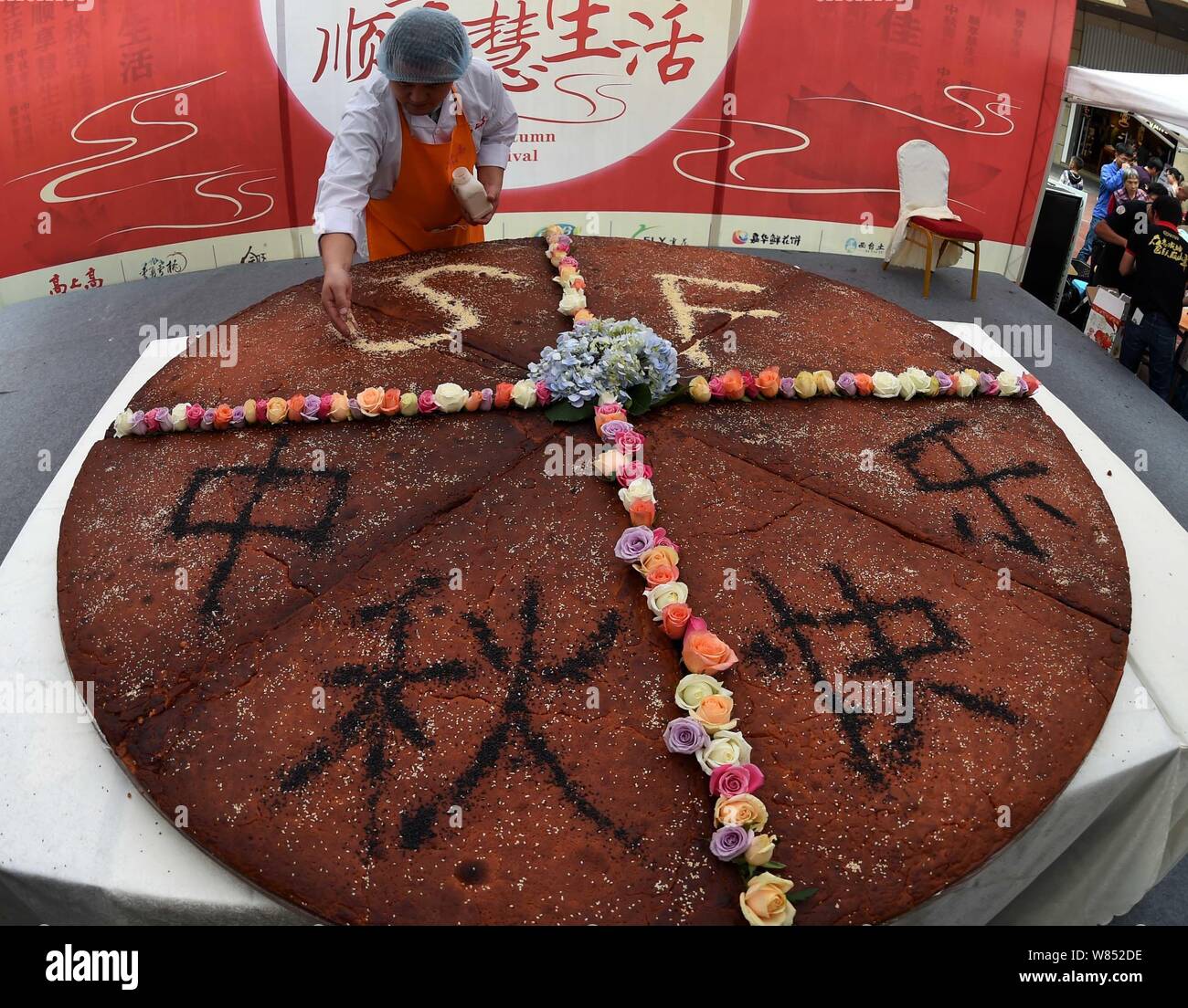 Un empleado de una empresa local de alimentos hace que los caracteres chinos con sésamo, que significa "Feliz Mid-Autumn Festival' en el mooncake gigante con un diámetro o Foto de stock
