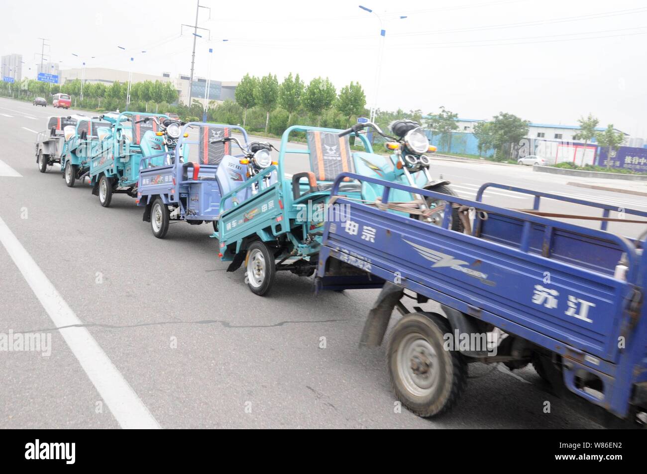 Un hombre chino monta un motor remolcando cinco triciclos triciclo eléctrico  en una carretera de Binzhou
