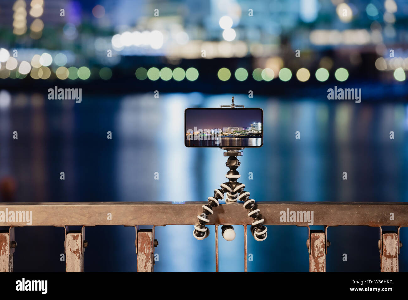 Usando el smartphone en el trípode flexible para hacer la foto de noche las luces de la ciudad Foto de stock
