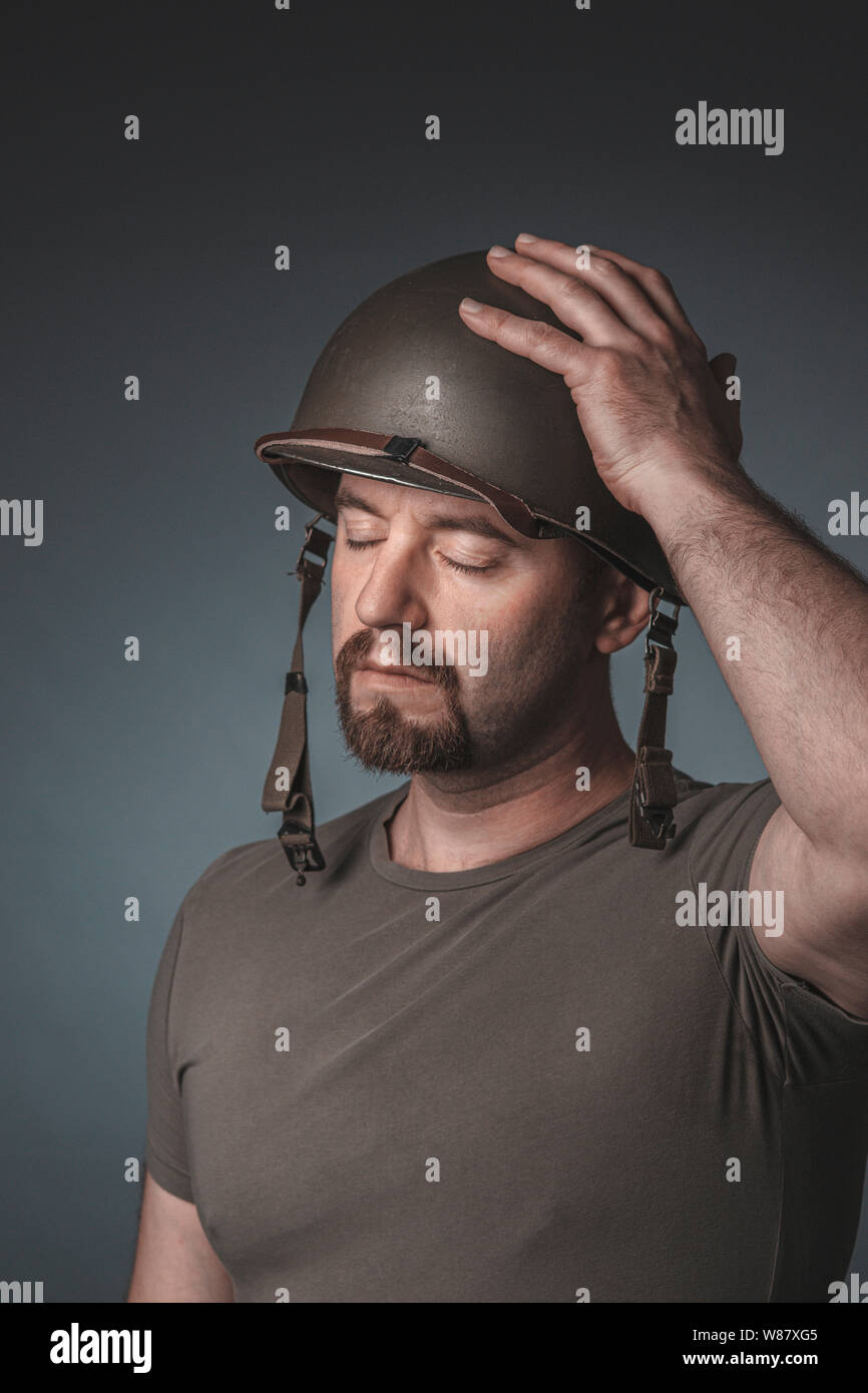 Retrato de un soldado con su mano sobre su casco y sus ojos cerrados, toma en el estudio. Foto de stock