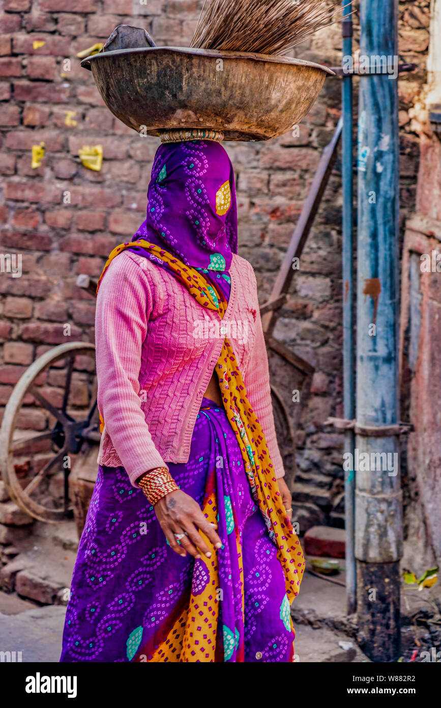 Barsana, India - Febrero 23, 2018 - Mujer viste de morado velo sobre su rostro mientras llevaba sus suministros en su cabeza Foto de stock