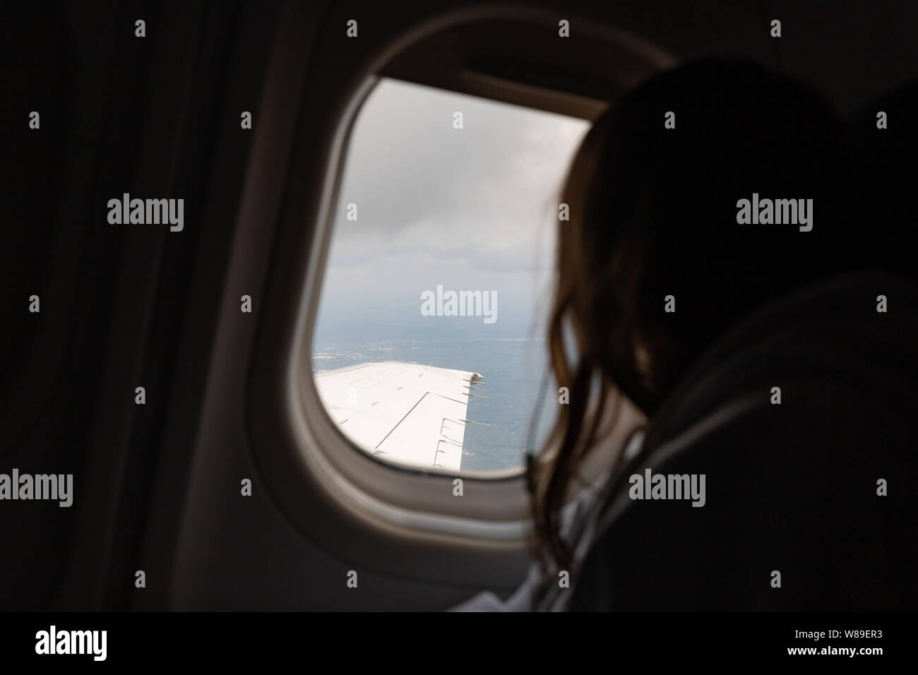 Chica mirando por la ventana del avión en vuelo mientras viaja Foto de stock