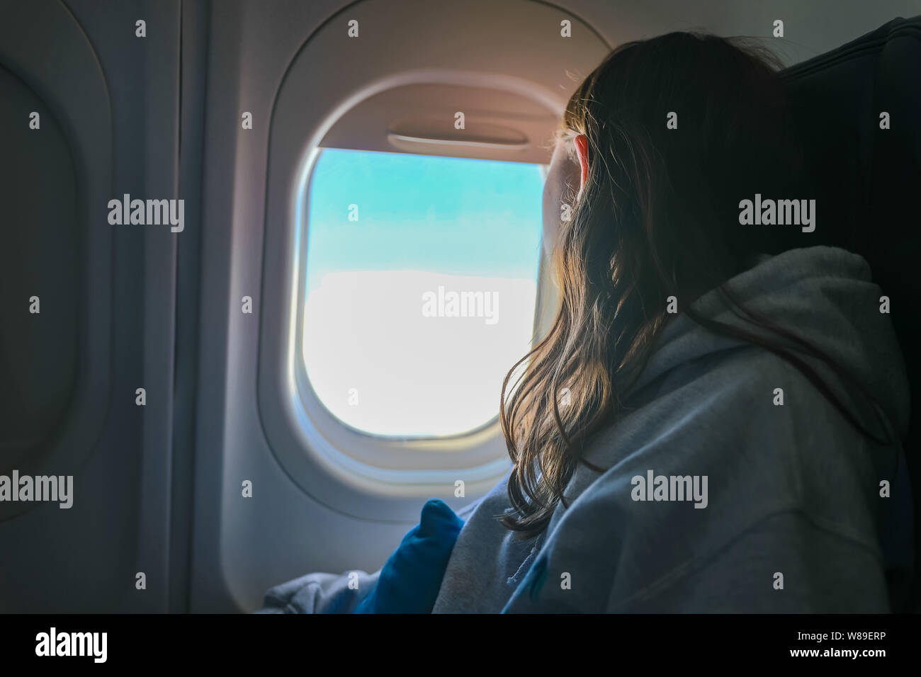 Chica mirando por la ventana del avión en vuelo mientras viaja Foto de stock